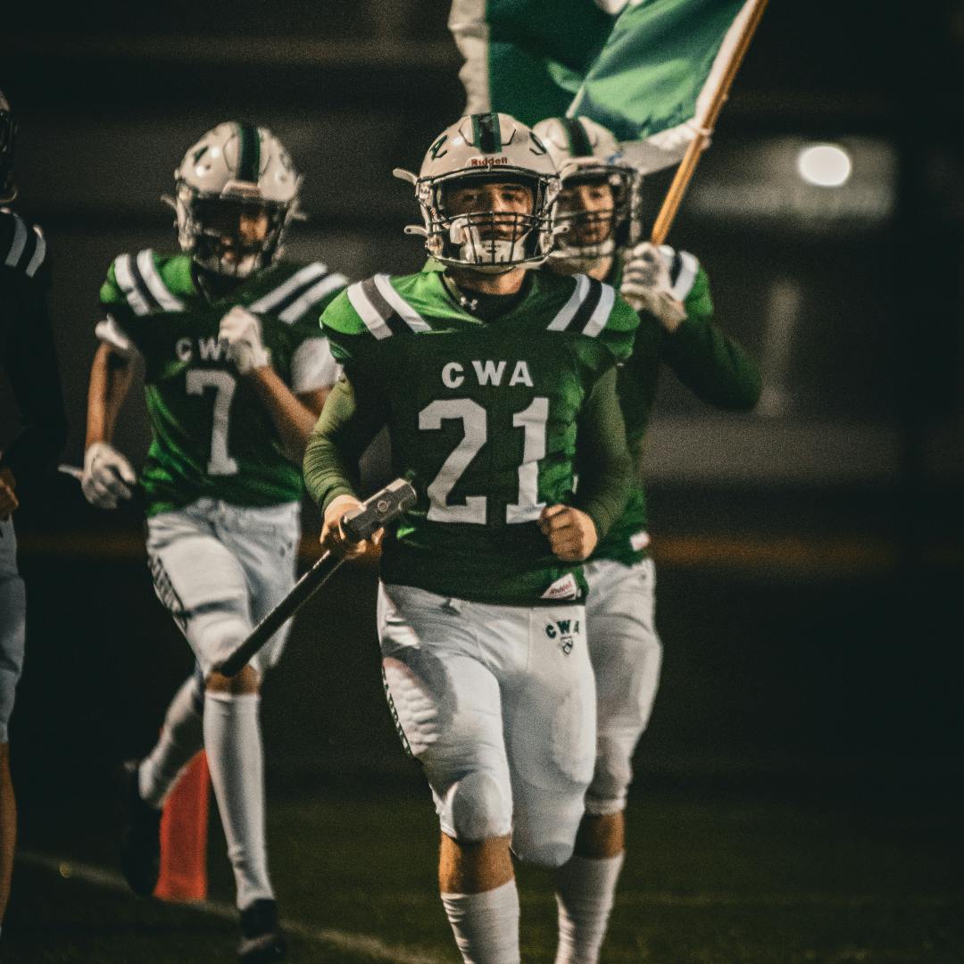 Football players in green and white uniforms running onto a field