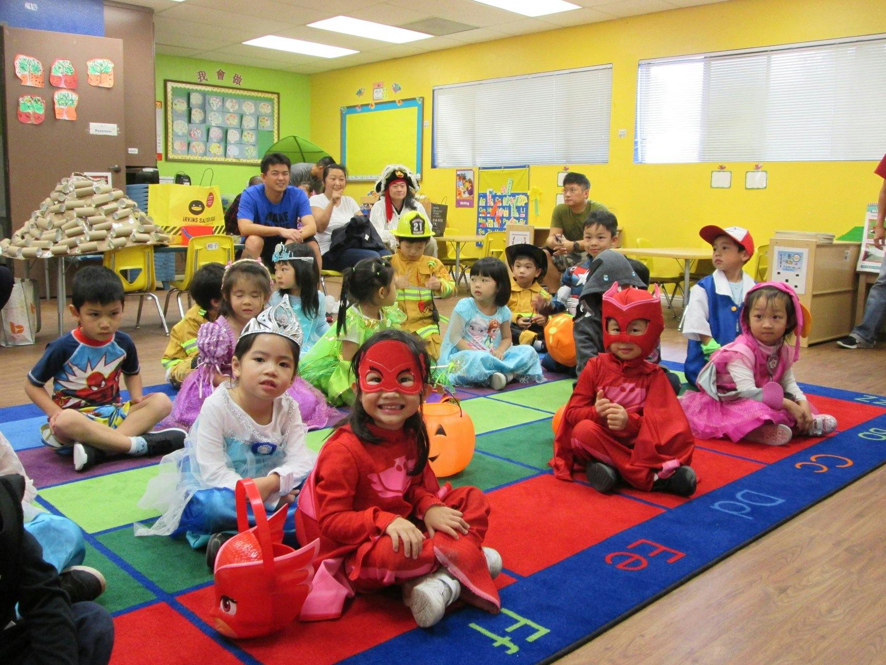 Children and adults in costumes sitting on a colorful rug in a classroom