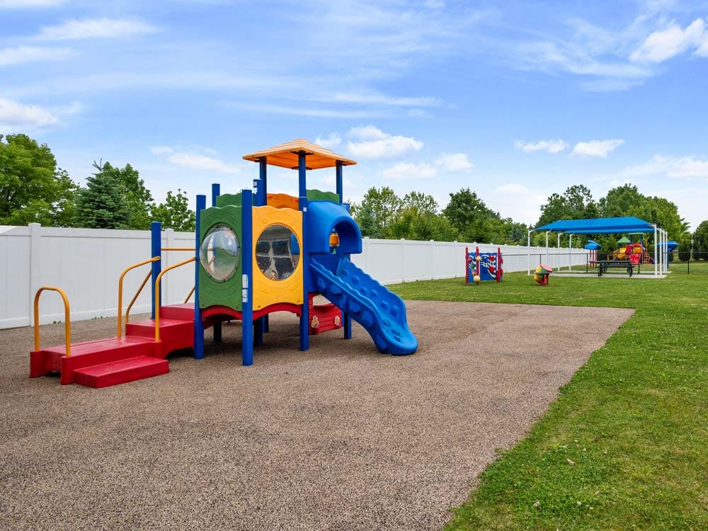 Colorful playground with slide, climbing structure, and fenced green area