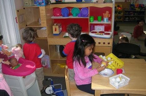 Children playing in a classroom with a play kitchen and toy eggs