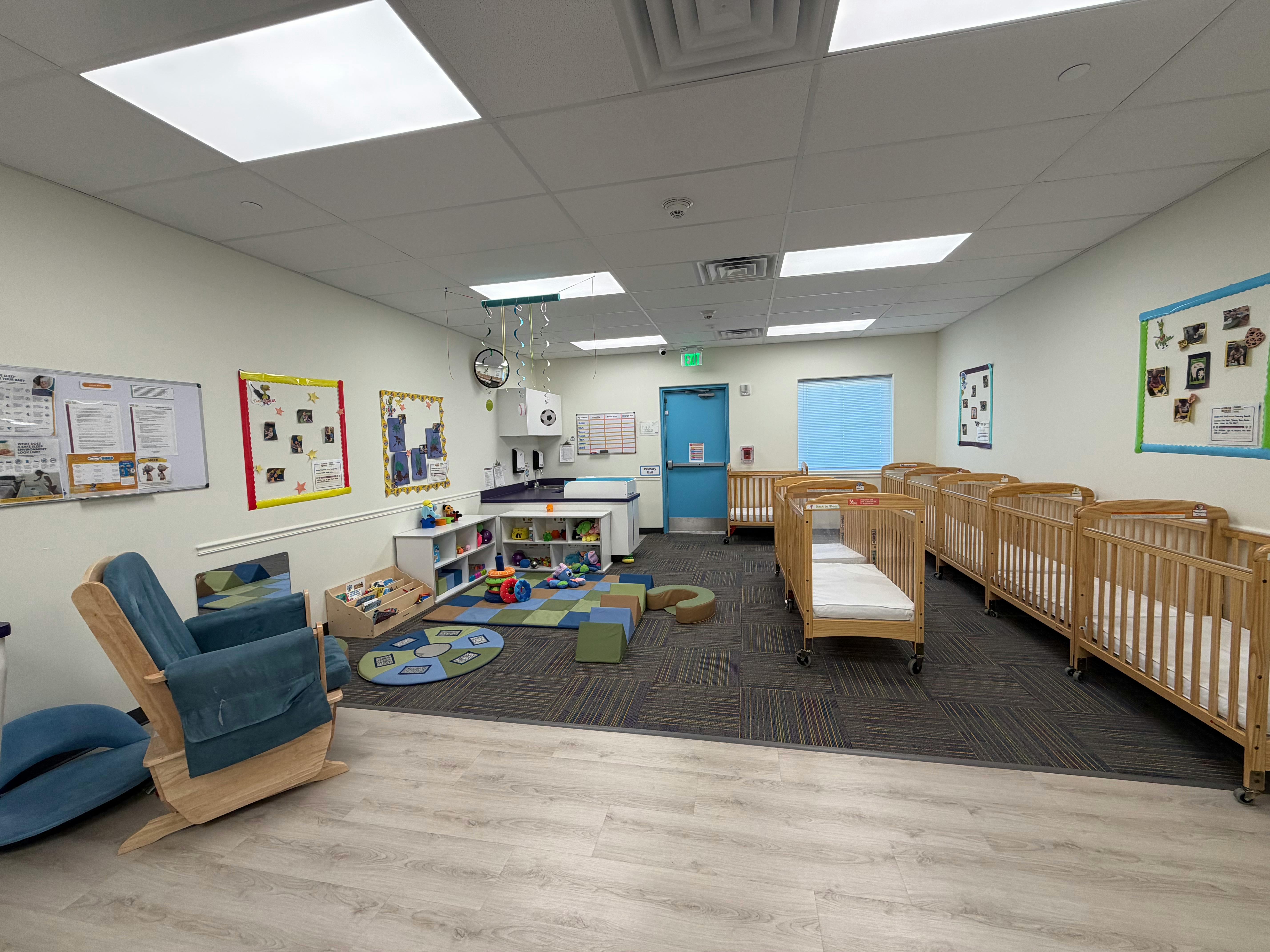 A room with several cribs and a play area with a rug with blocks on the floor