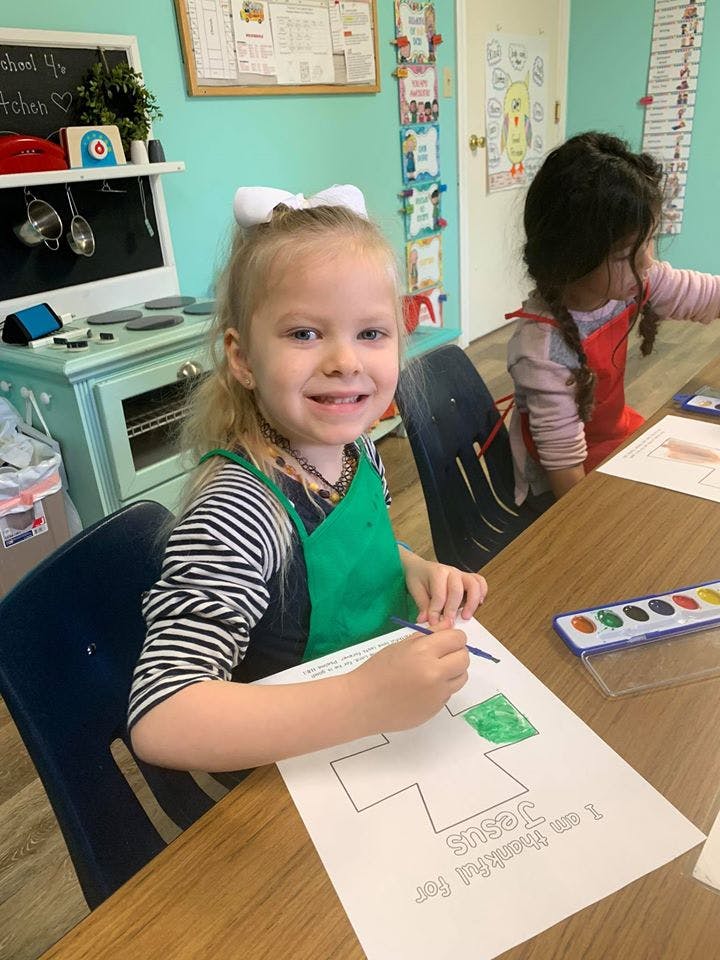 Child painting a cross on paper at a table