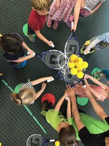 Children holding tennis rackets and balls in a circle