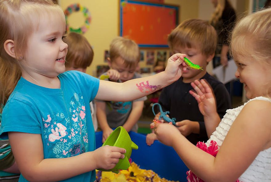 Child holding a green toy to another child's face in a classroom