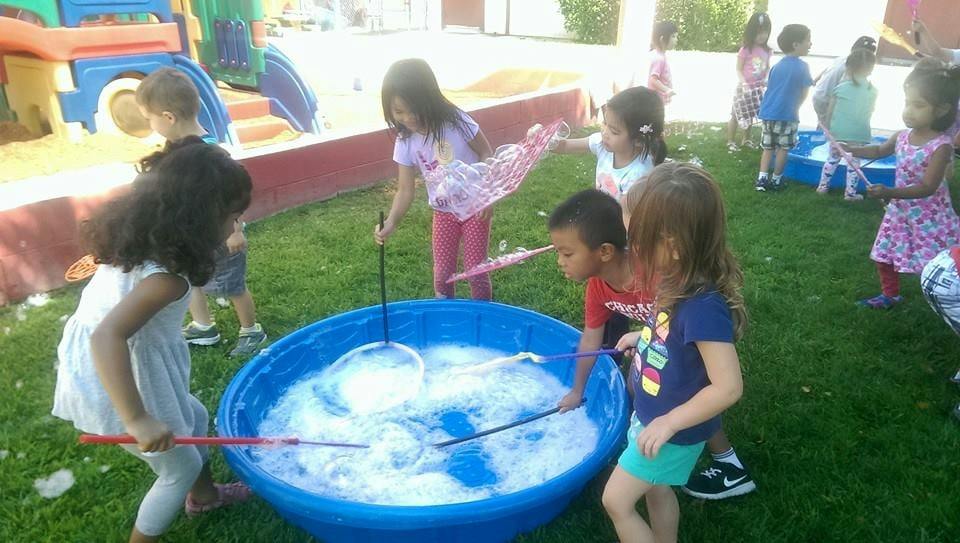 Children playing with bubbles in a blue tub outdoors