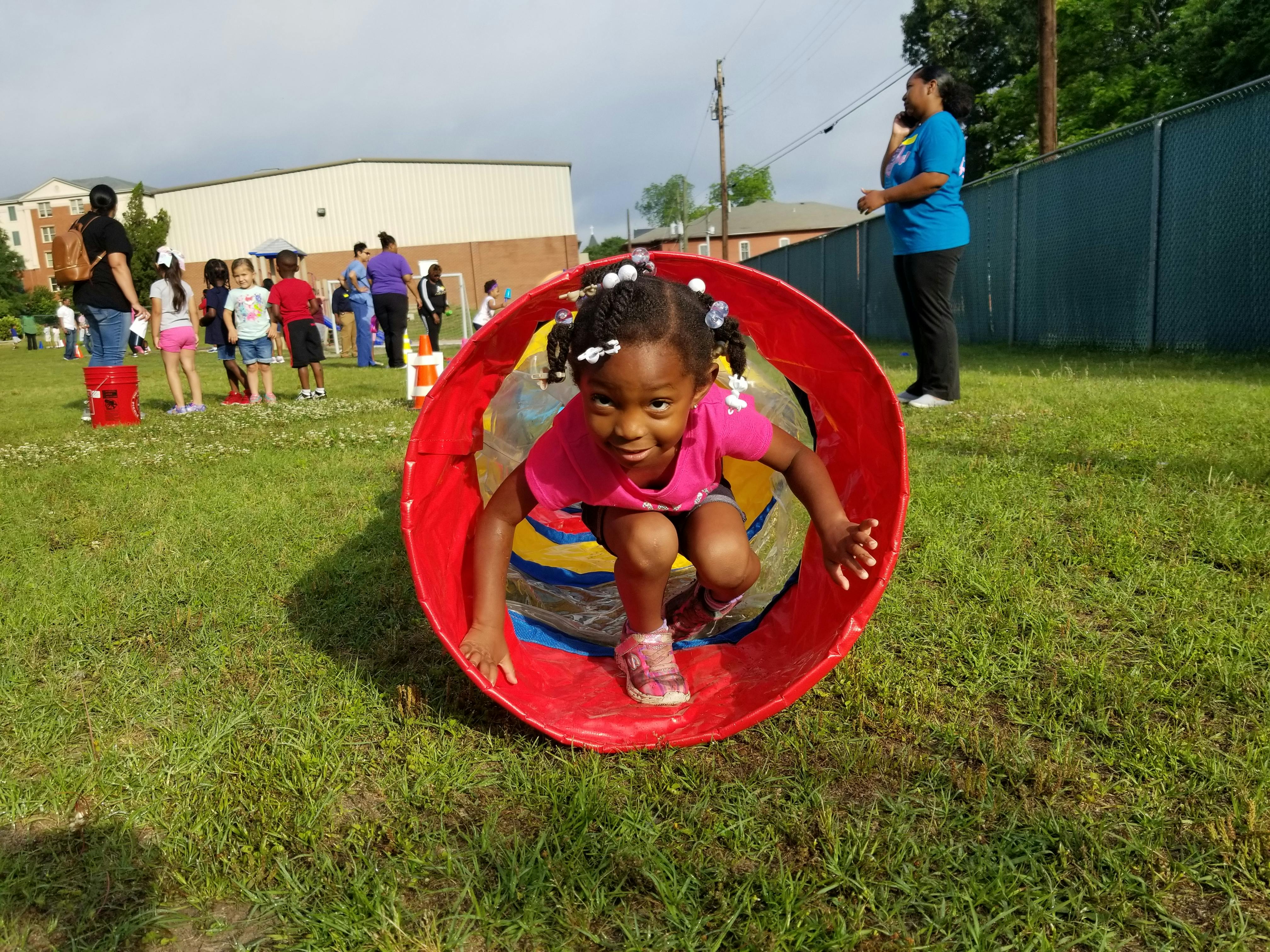 Child crawling through a red tunnel on grass