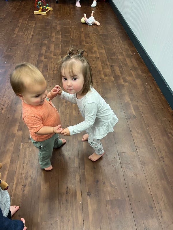 Two children holding hands while standing on a wooden floor