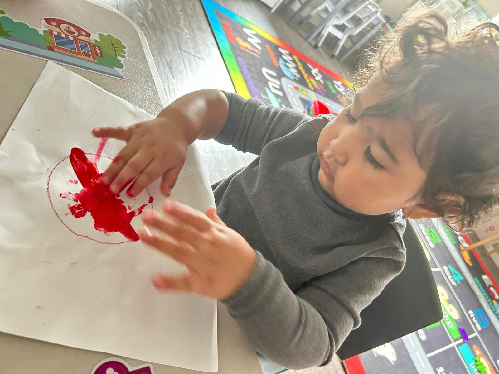 Child pressing hands into red paint on paper