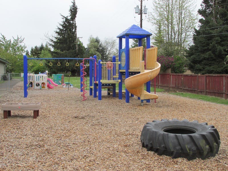 Playground with slides, swings, and a large tire on wood chips