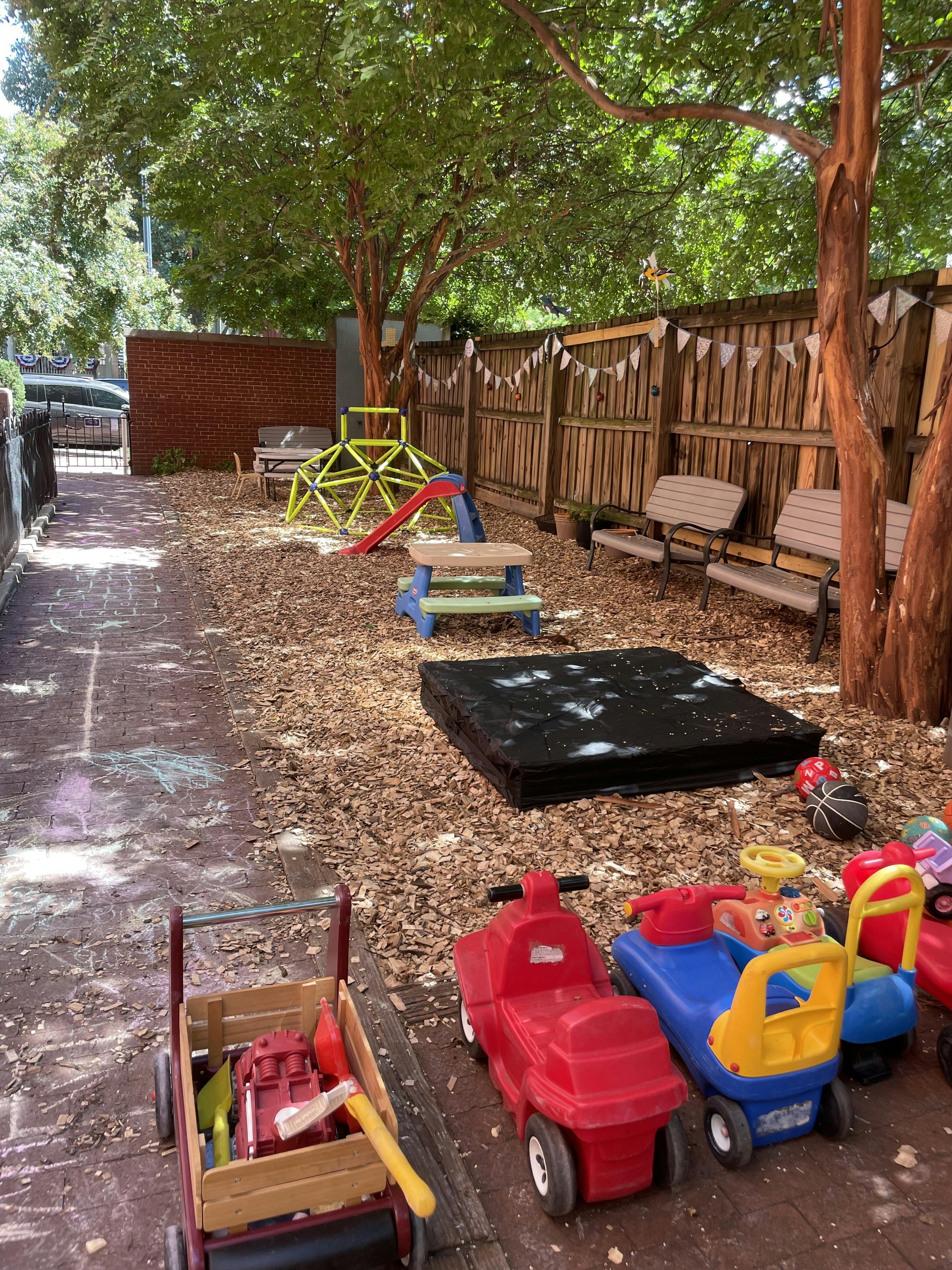 Outdoor playground with climbing dome, slide, sandbox, and ride-on toys