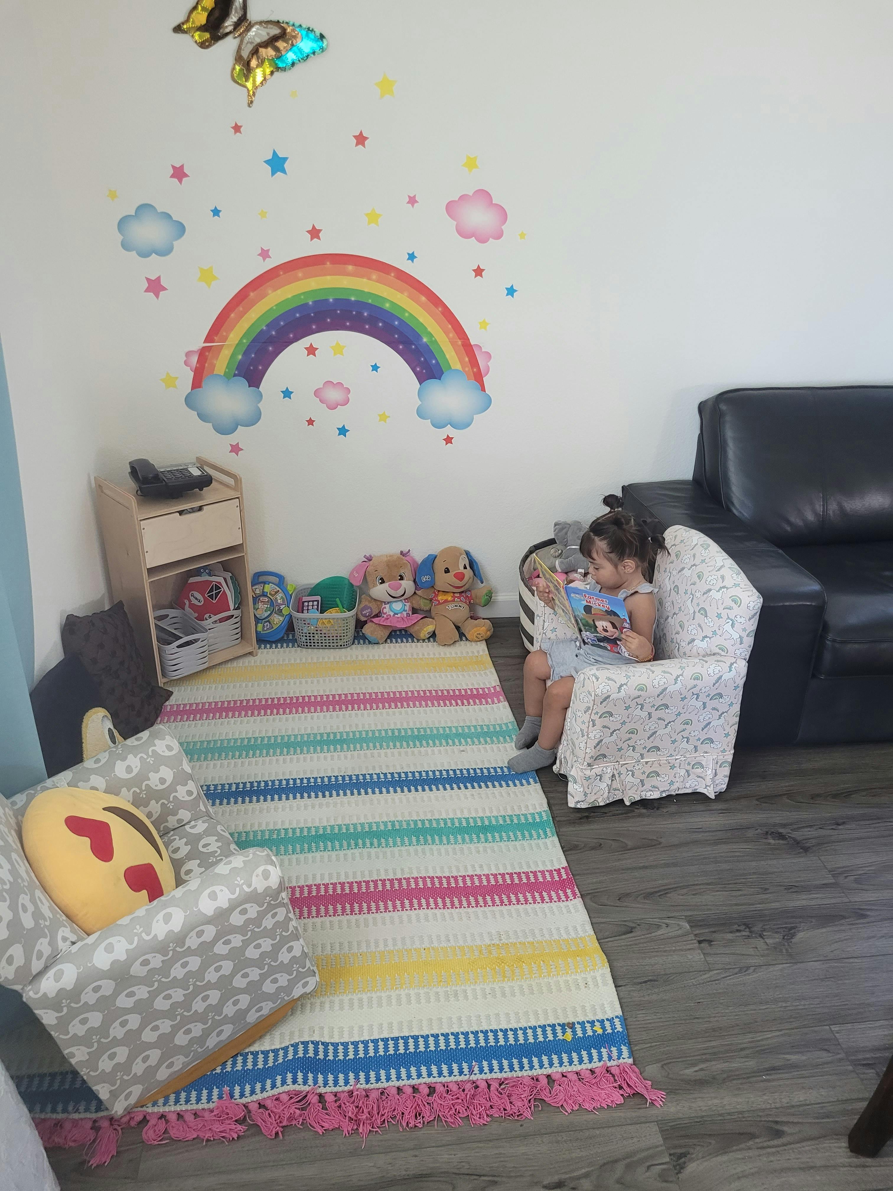 Child sitting in a chair reading a book in a room with a rainbow wall decal