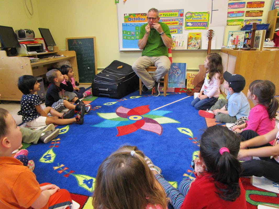 Adult playing harmonica for children sitting on a rug in a classroom
