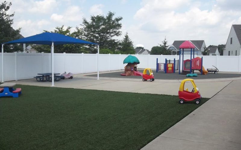 Outdoor playground with artificial turf, play structures, and small ride-on cars
