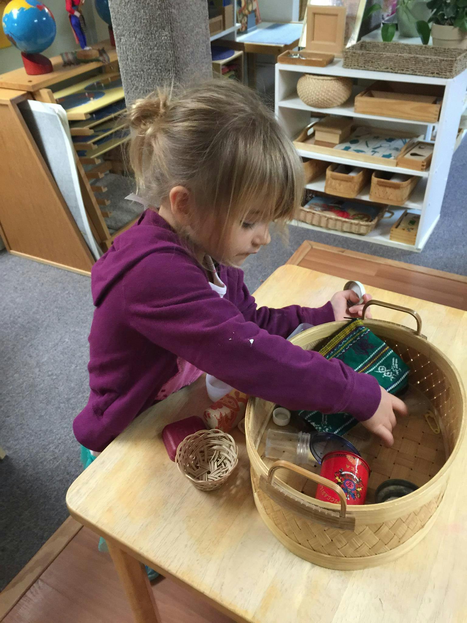 Child in a purple hoodie reaching into a basket on a wooden table