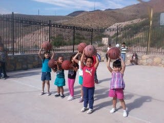 Children holding basketballs over their heads on a paved court