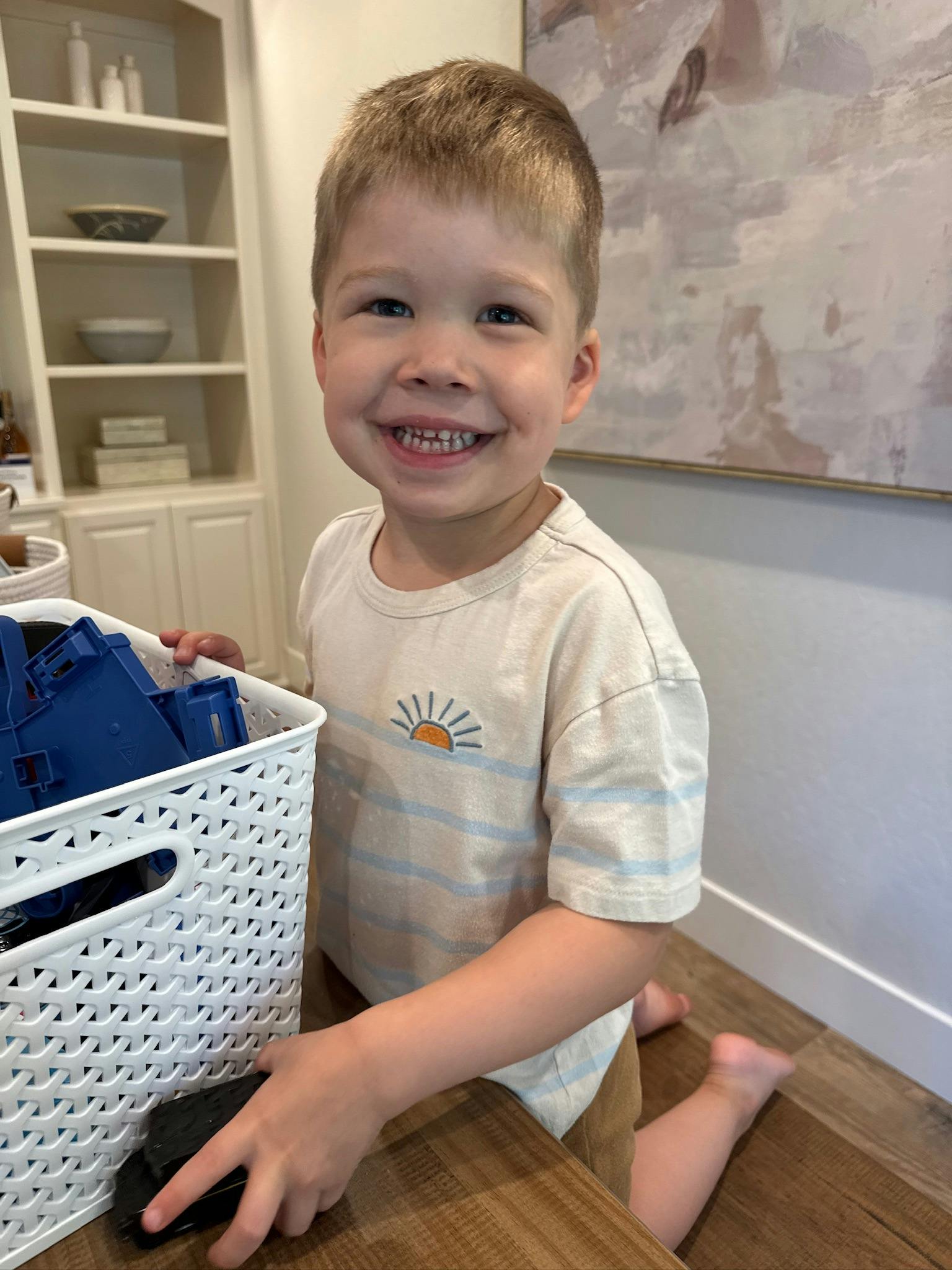 Child kneeling next to a white basket, smiling