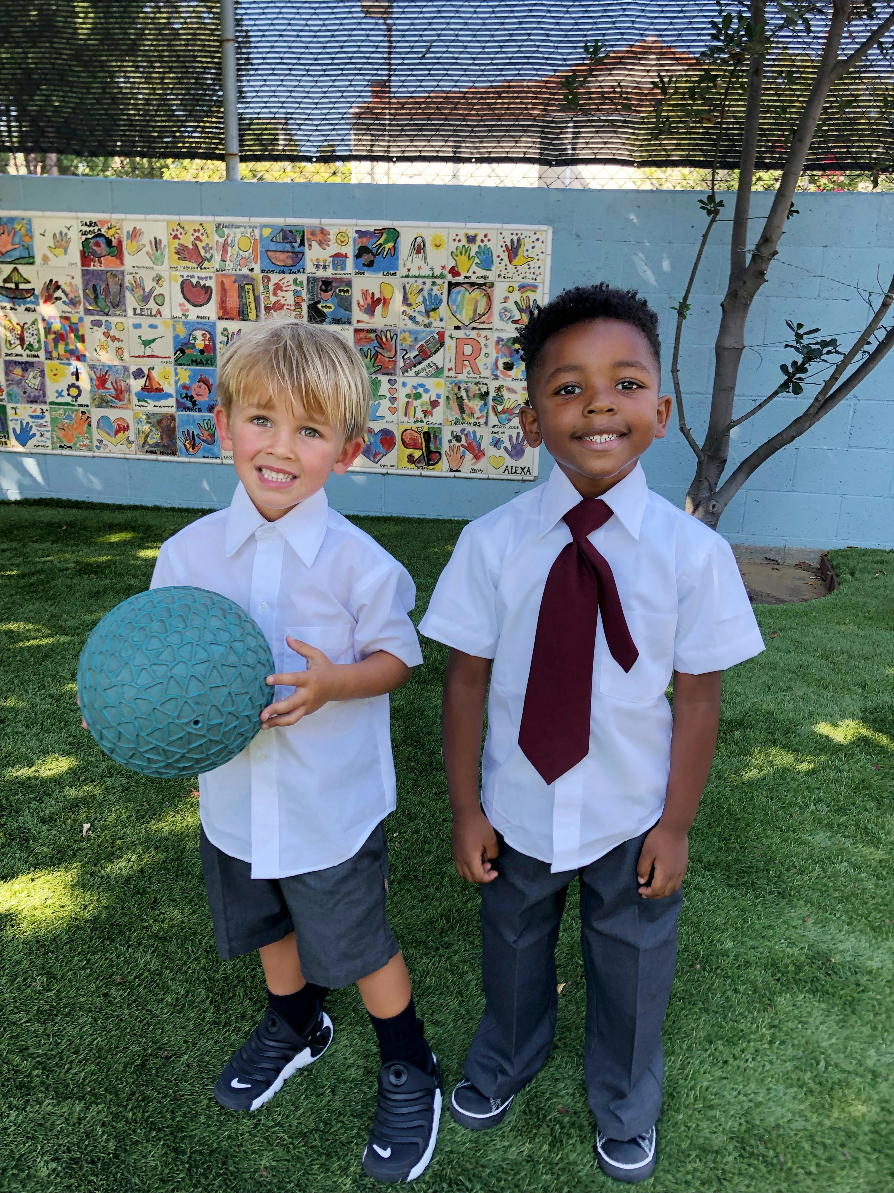 Two children in school uniforms, one holding a ball