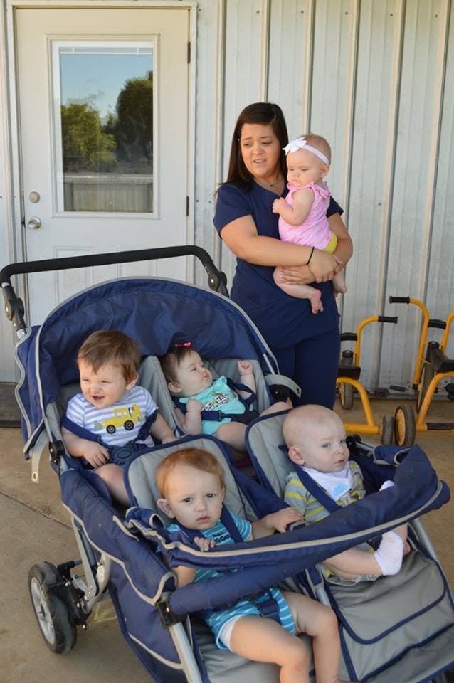 Person holding a child, with four other children in a multi-seat stroller