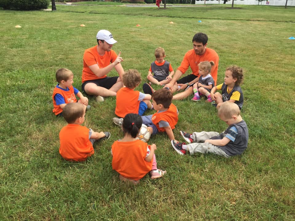 Two people and several children sitting in a circle on grass