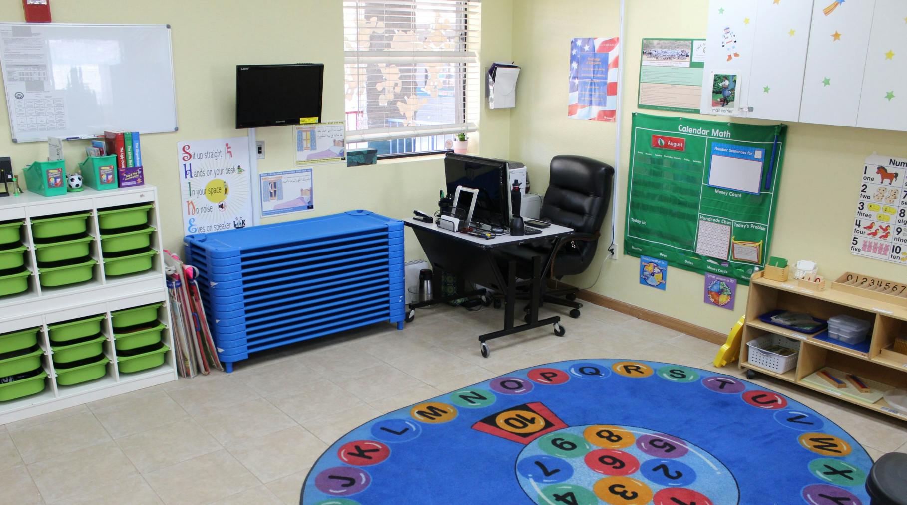 Classroom with a blue rug, desk, and storage shelves