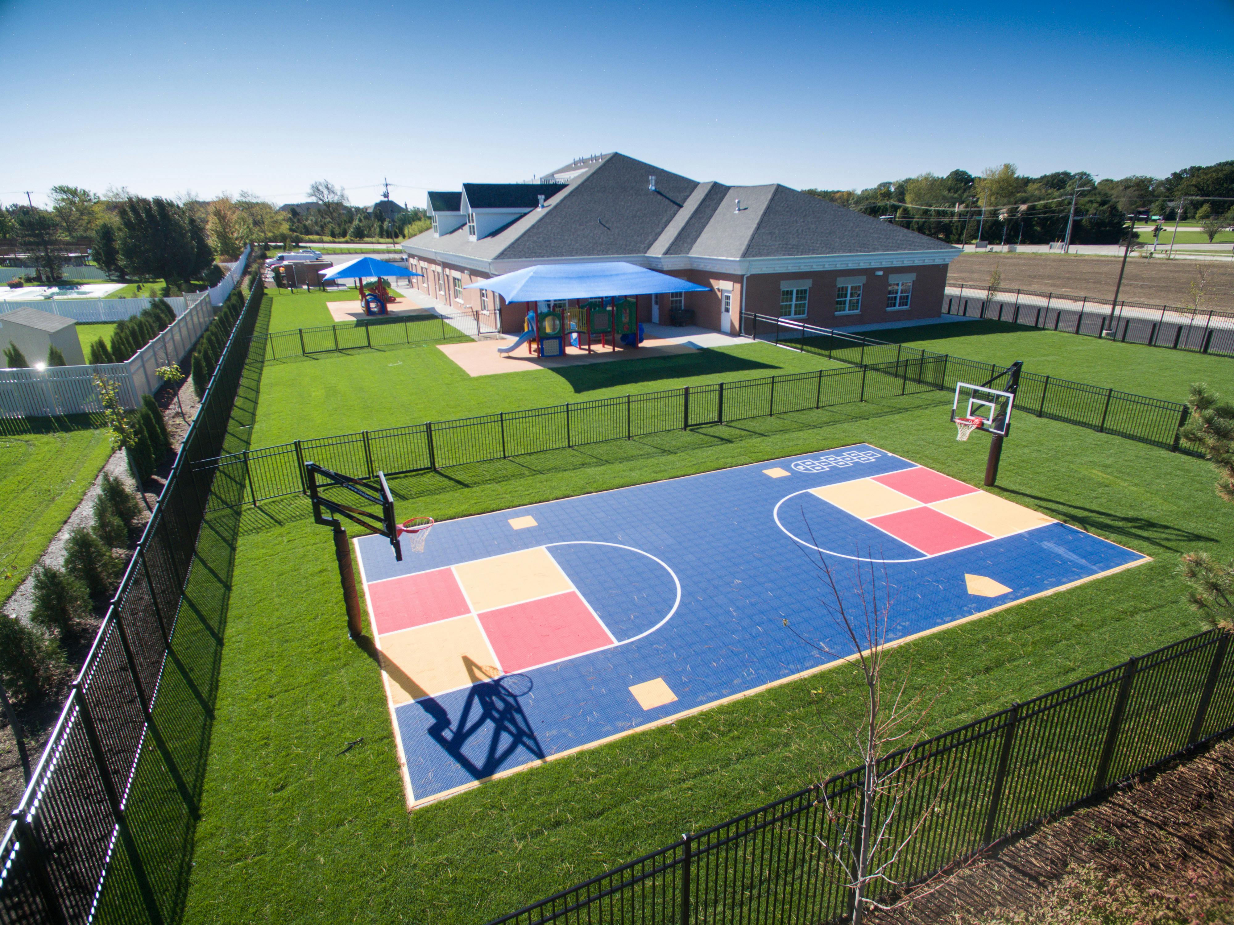 Outdoor basketball court with a building and playground in the background