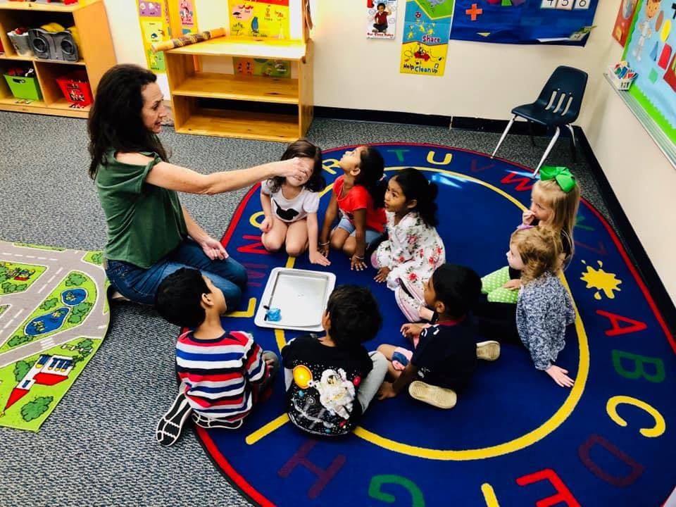 Person interacting with children sitting on a rug in a classroom