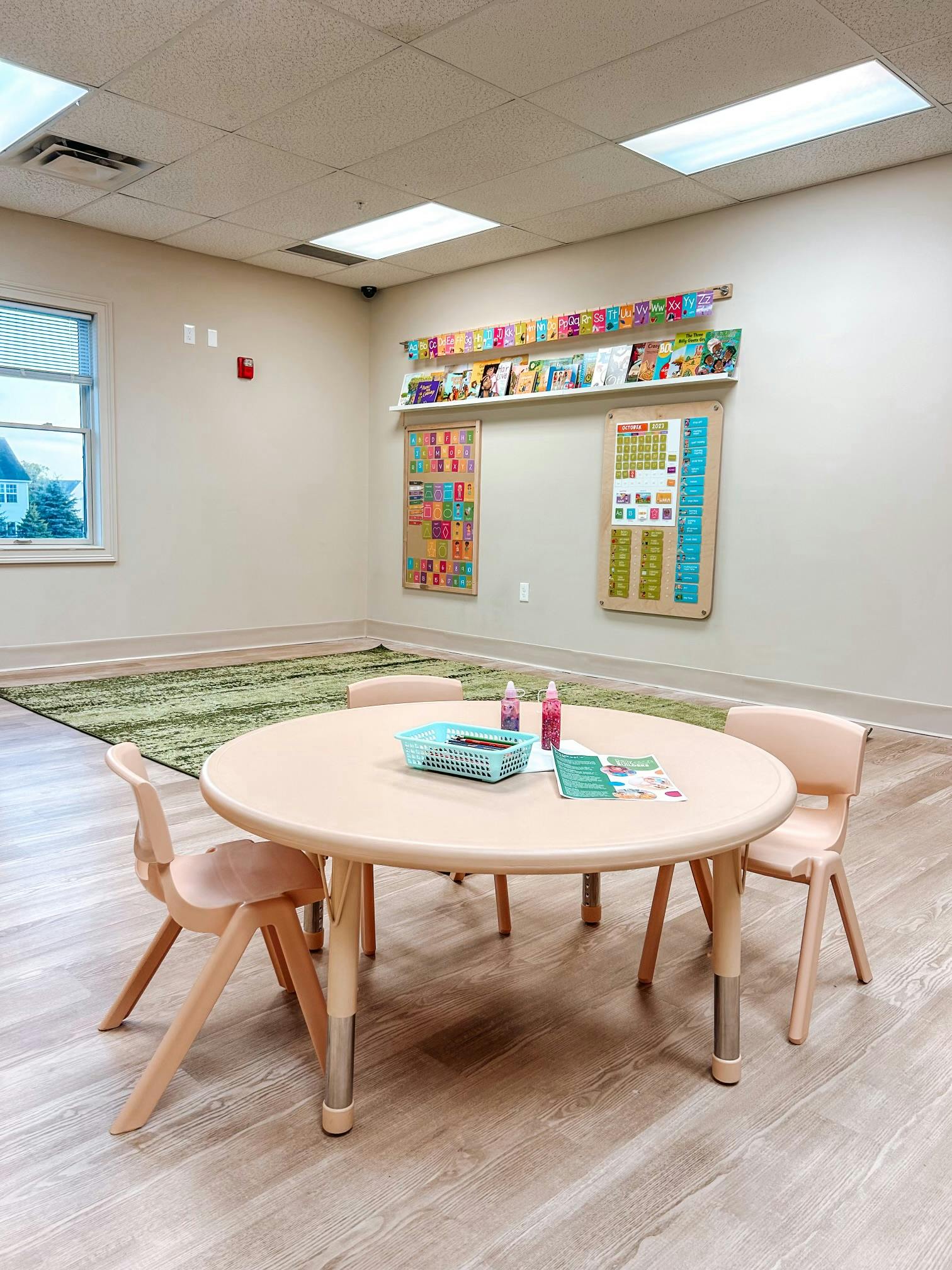 Classroom with a round table and chairs, green rug, and educational posters on the wall