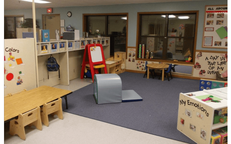 Empty classroom with small tables and chairs, play equipment, and learning displays