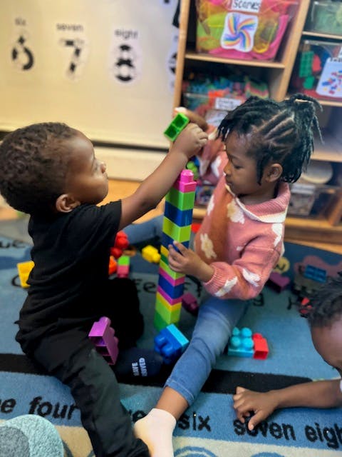 Two children building a tower with colorful blocks on a rug