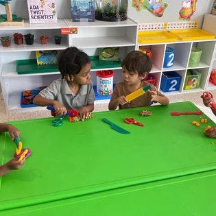 Two children playing with toys at a green table