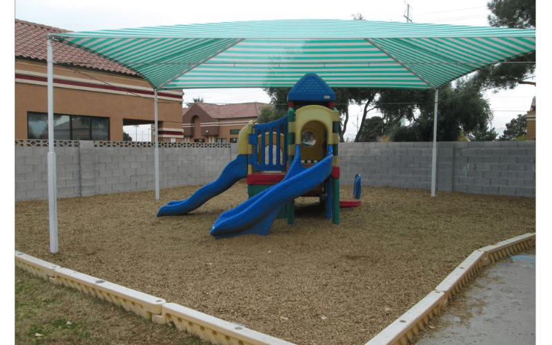 Playground structure with slides and a striped shade canopy over wood chips