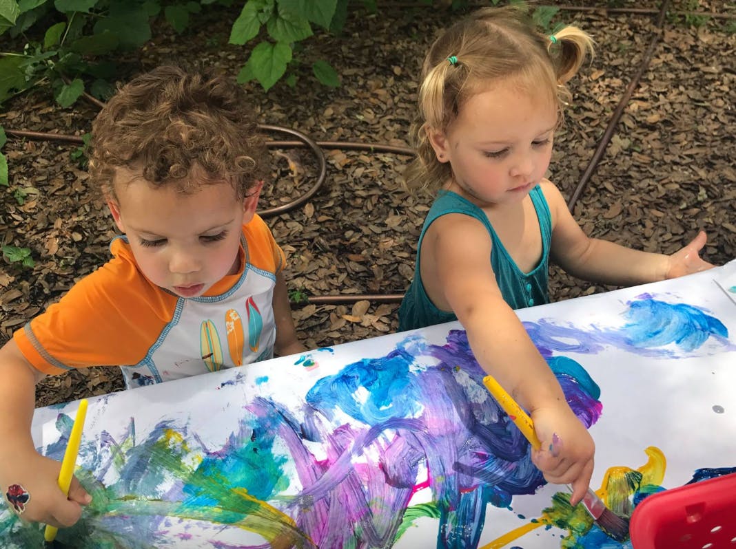 Two children painting on a large sheet of paper outdoors