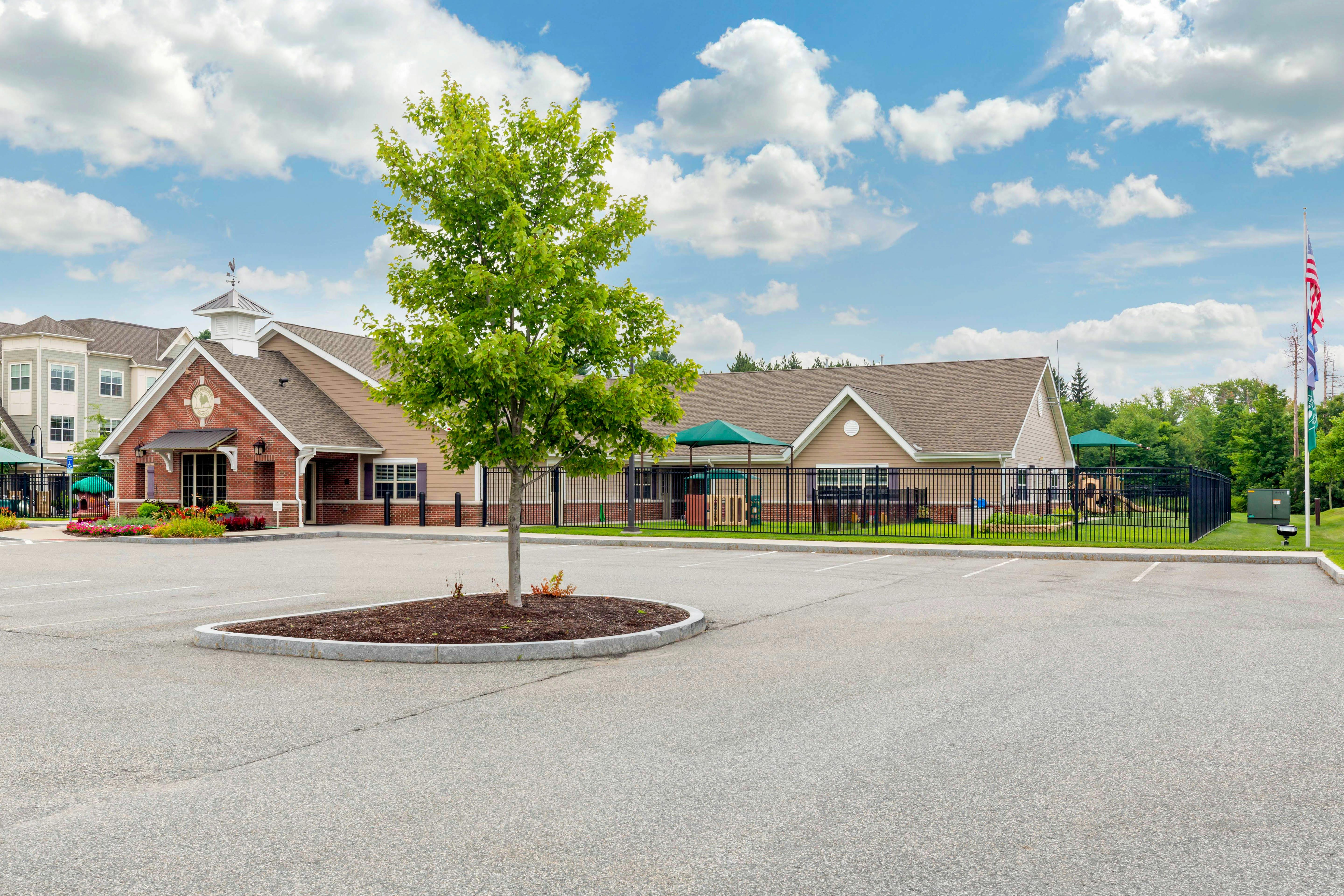 Building with a weather vane, a parking lot, and a fenced playground area