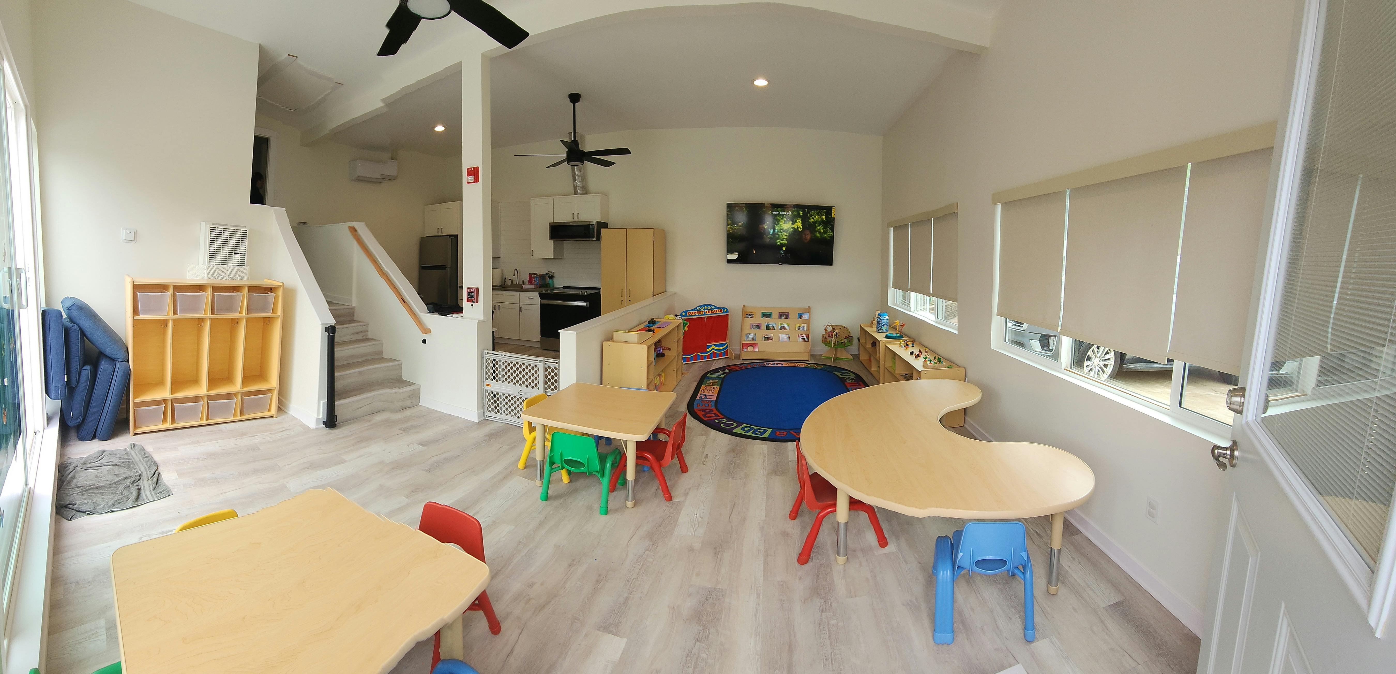 Classroom with small tables and chairs, cubbies, and a play area