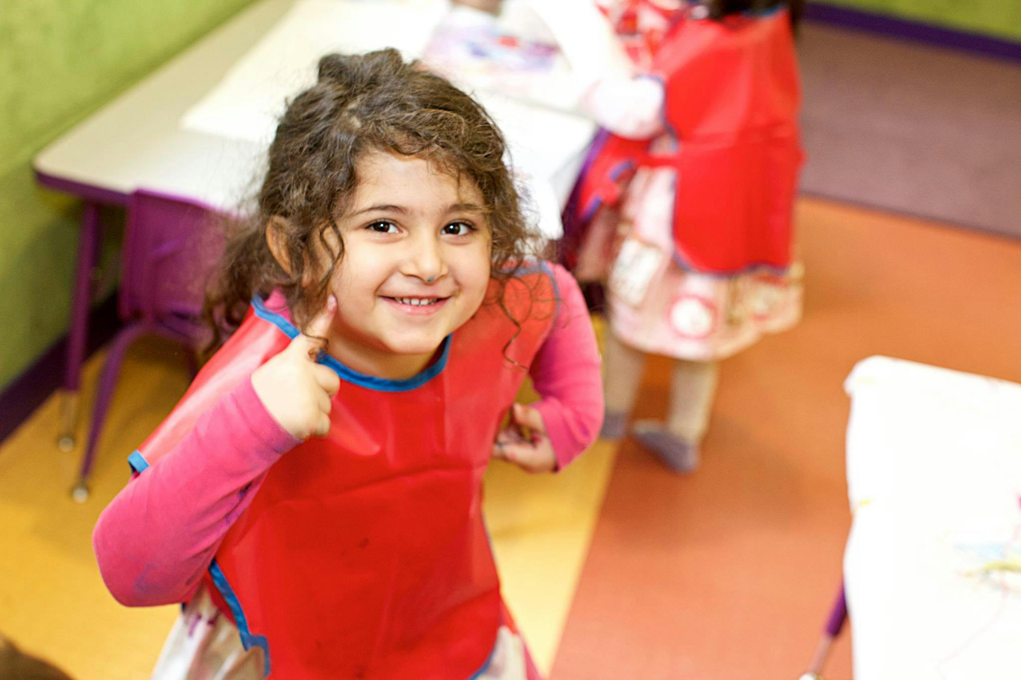 Child in a red smock giving a thumbs up