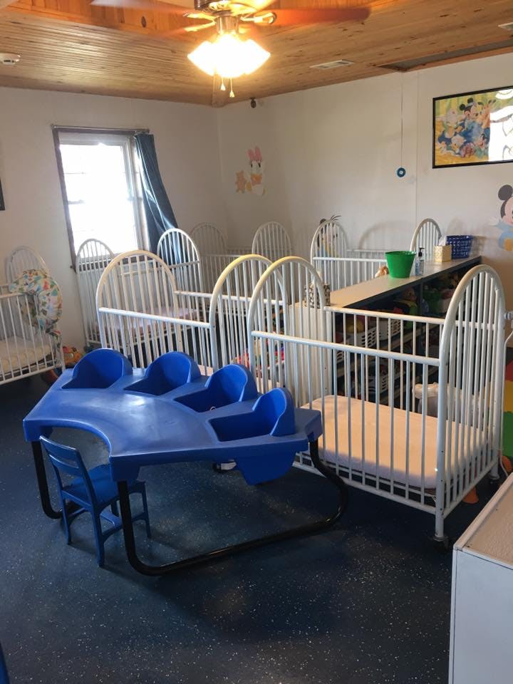 Multiple white cribs and a blue children's table with chairs in a room