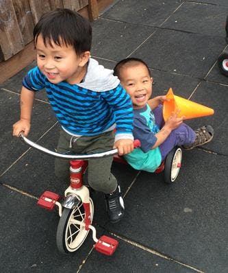 Two children playing with a tricycle and a toy car