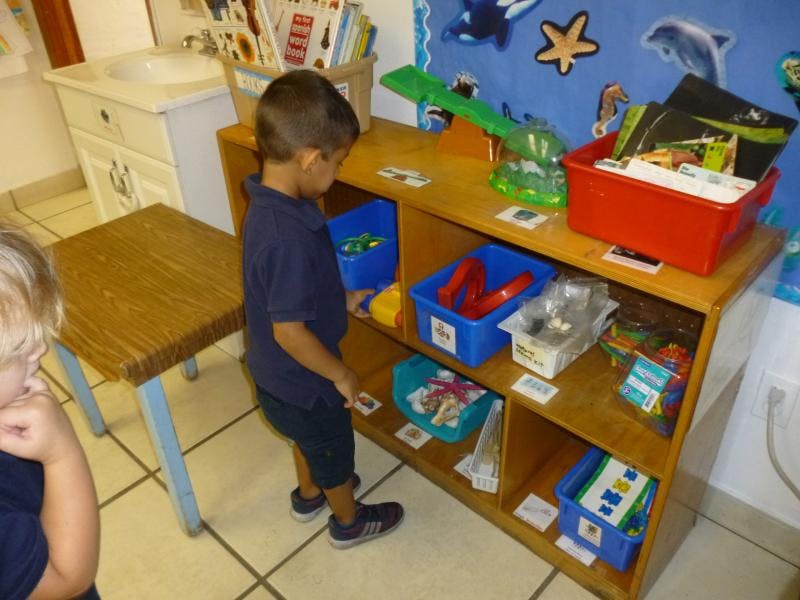 Child standing next to a wooden shelf with toys