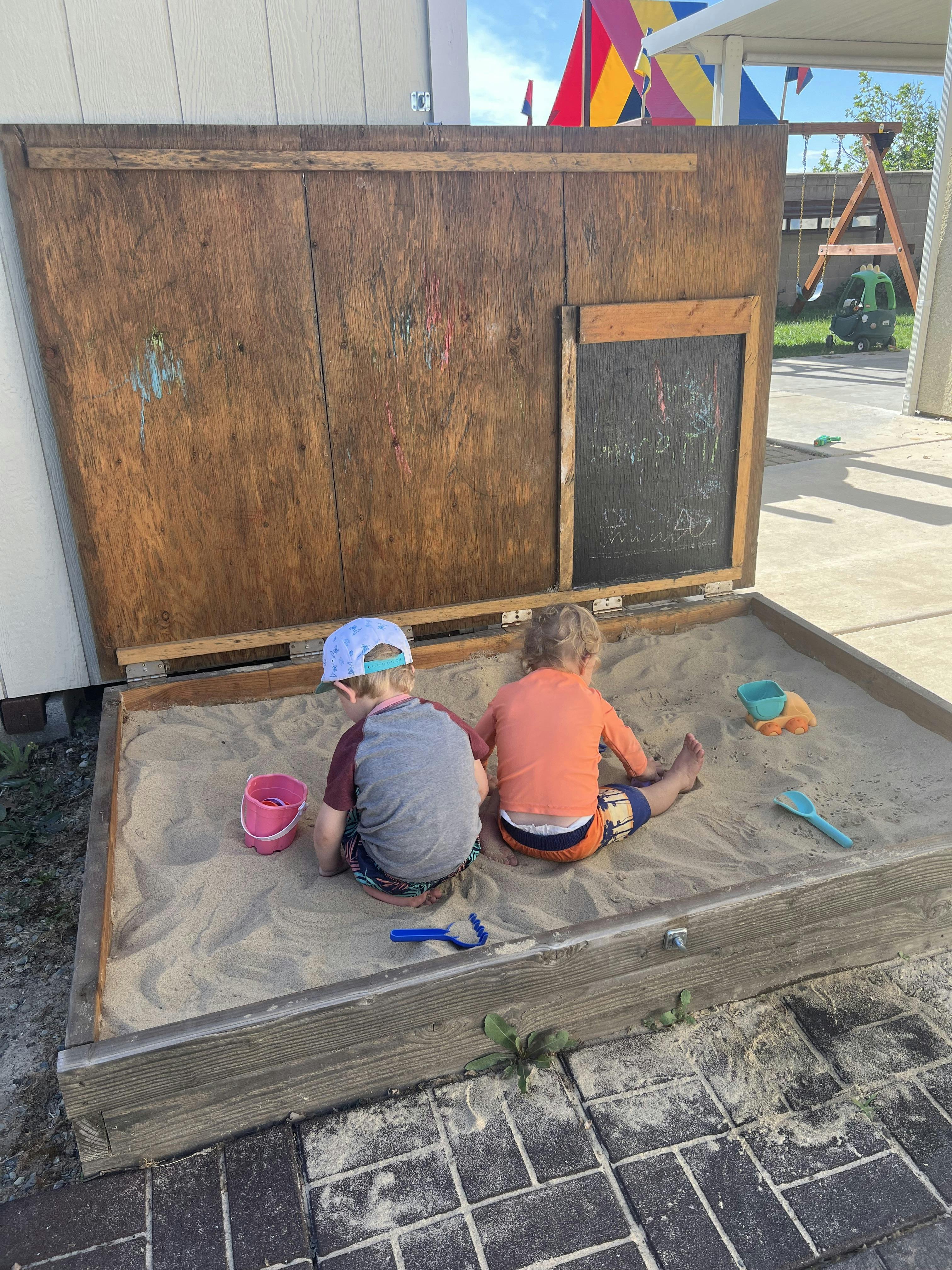 Two children playing in a wooden sandbox with sand toys