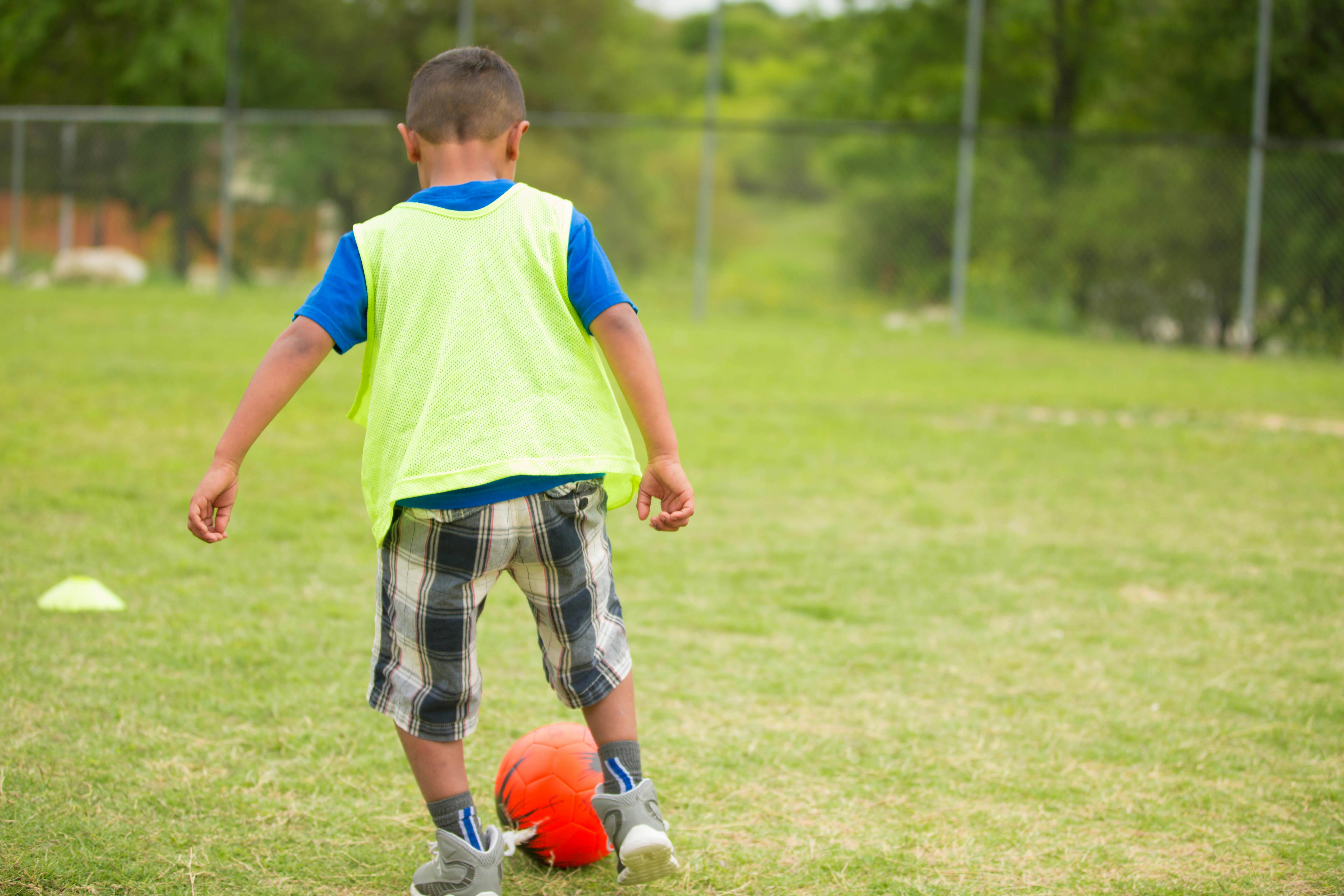 Child in a neon vest kicking a soccer ball on a grassy field