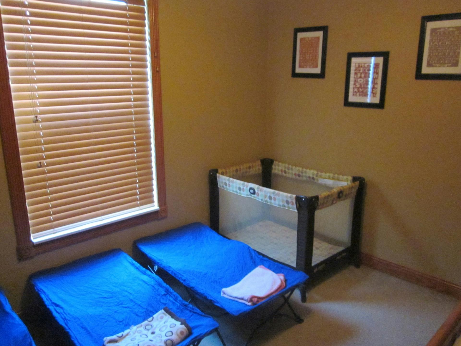 Two blue cots and a playpen in a room with a window