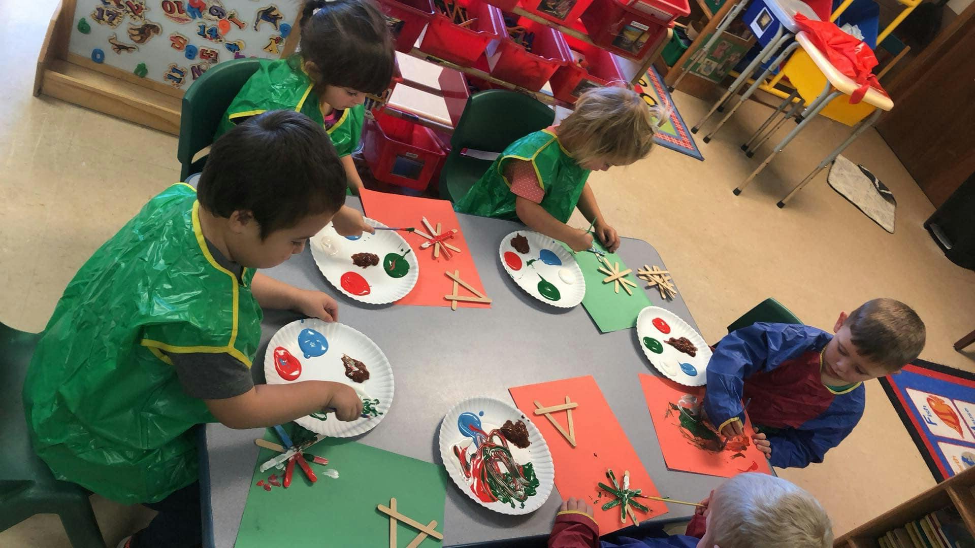 Children painting and crafting at a table in a classroom