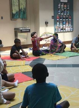 Child holding a colorful beaded structure while sitting on a mat with other children