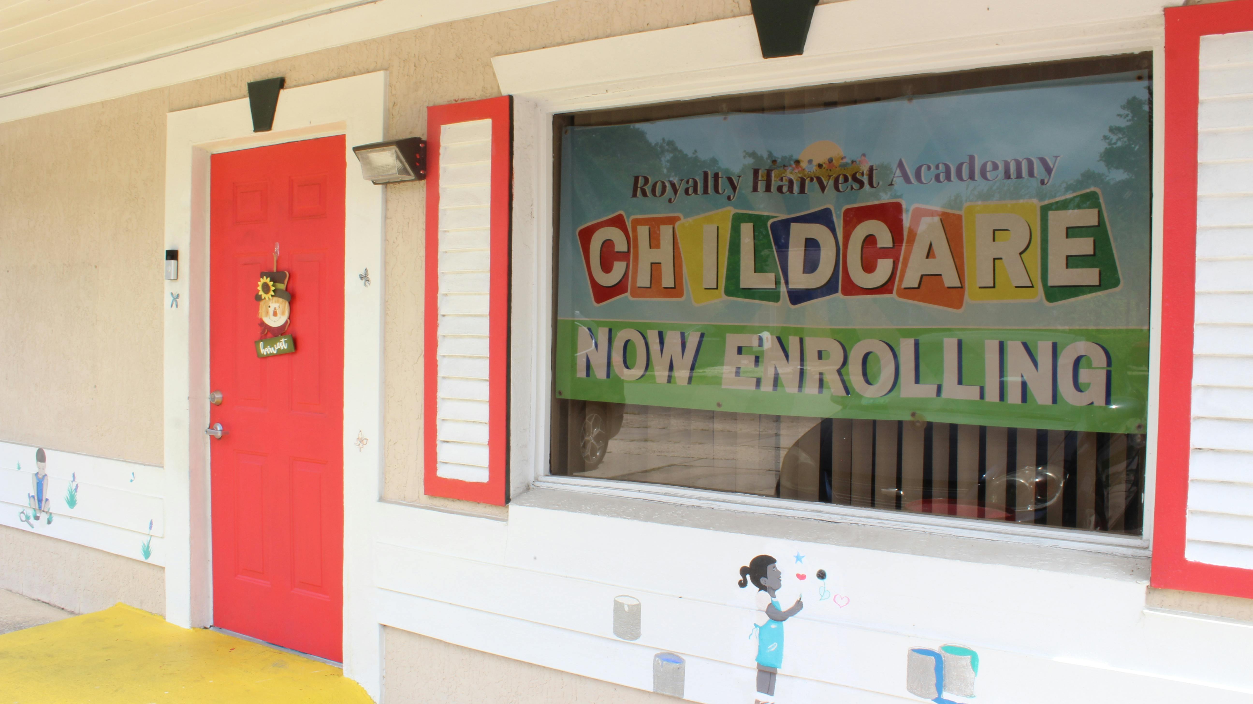 Building exterior with red door and window sign reading "Childcare Now Enrolling"