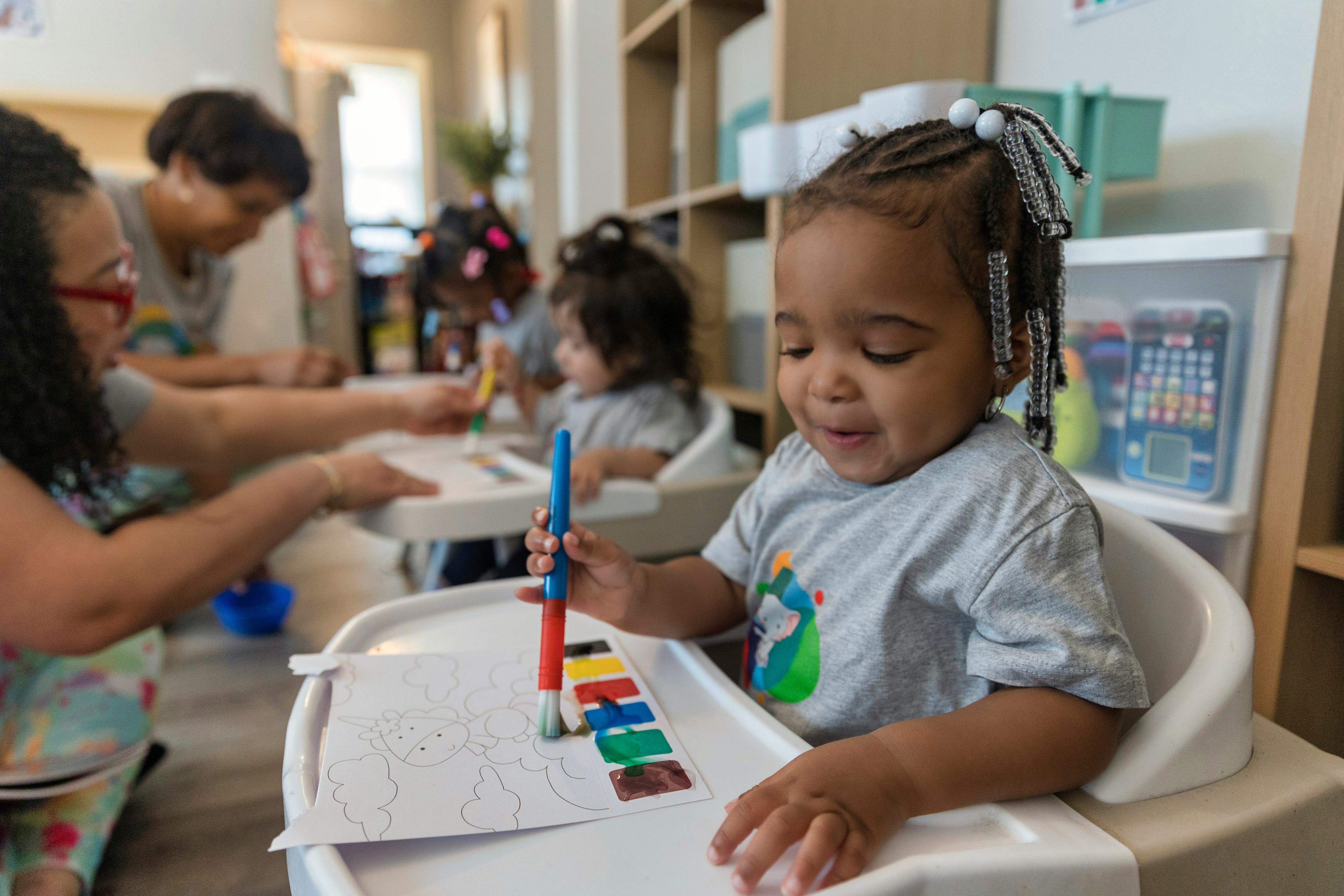 Child in a high chair painting with a brush and colorful paints