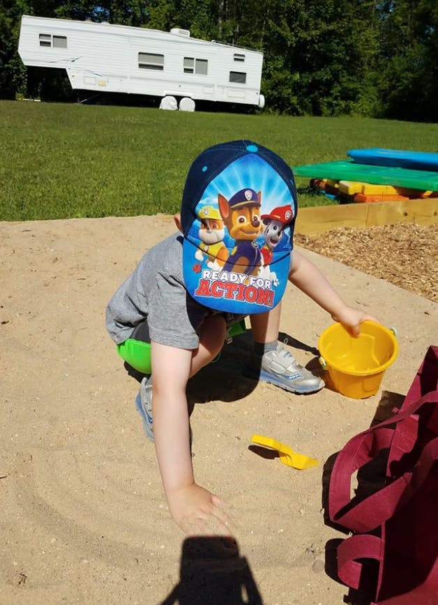 Child in a Paw Patrol hat playing in a sandbox with a yellow bucket