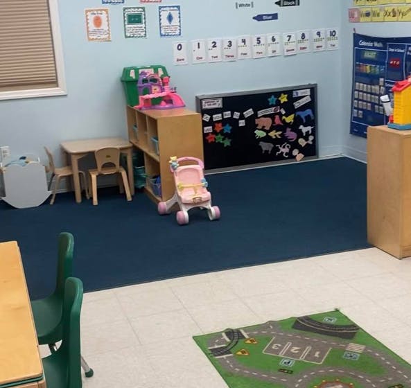 Classroom with small tables, chairs, toy stroller, and chalkboard with a rug on the floor