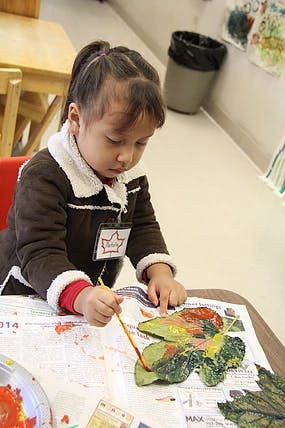 Child painting leaves at a table
