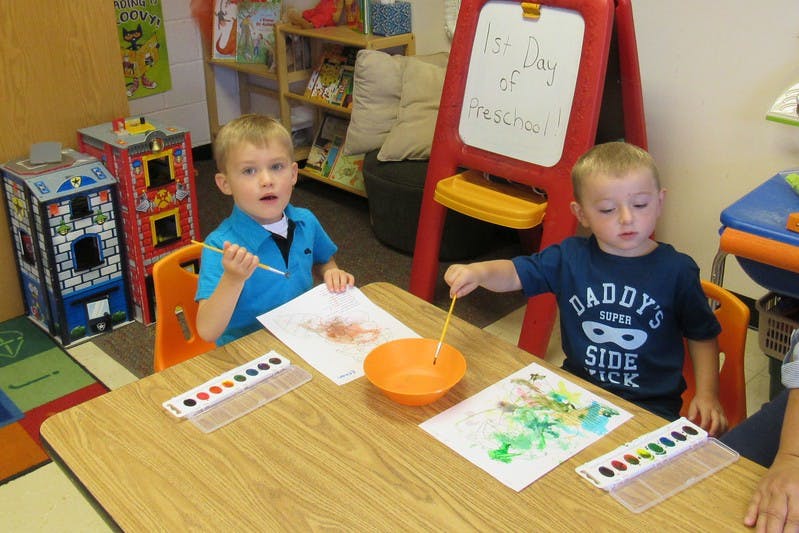 Two children painting at a table in a classroom