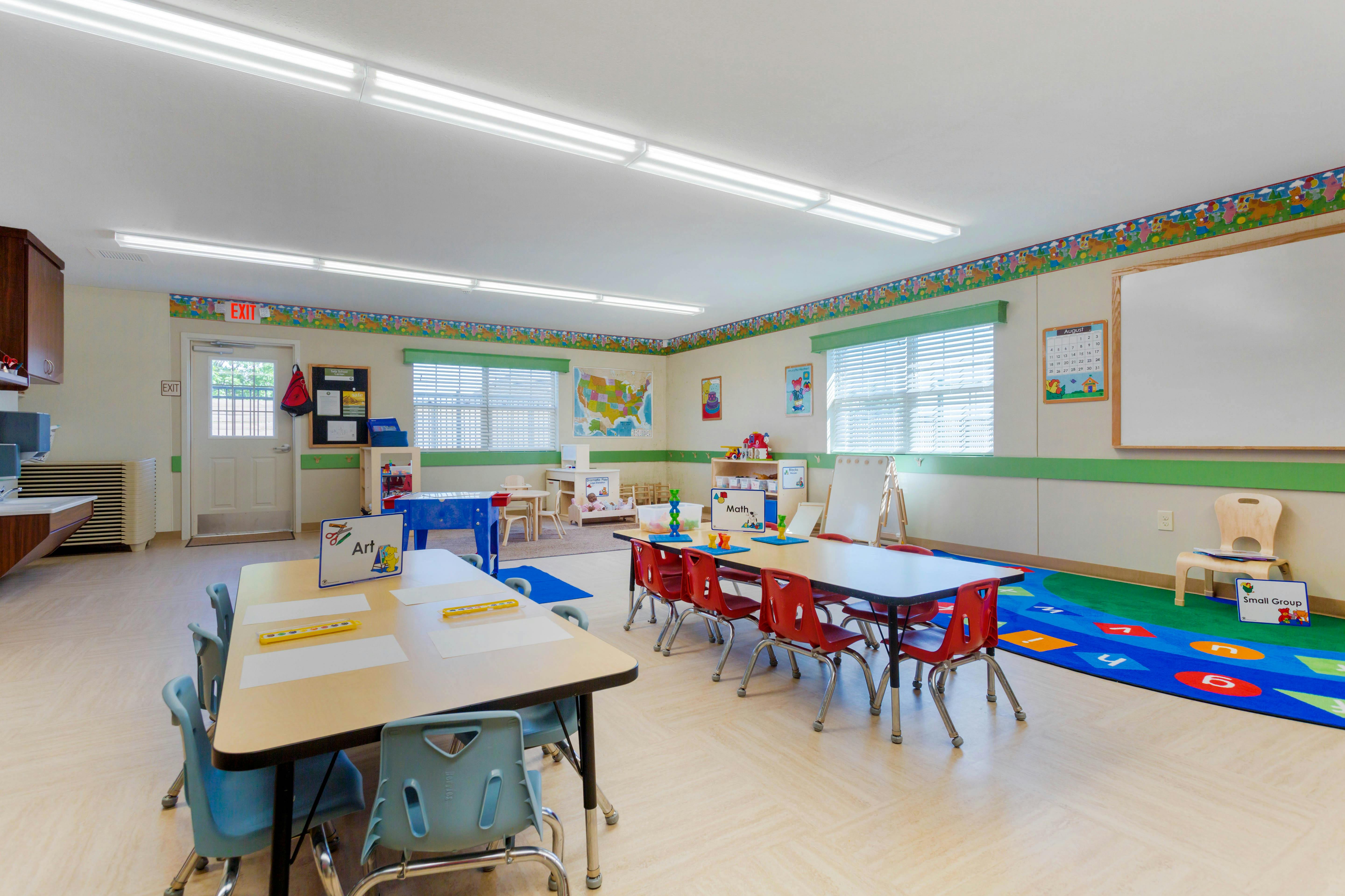 Classroom with child-sized tables and chairs, a play area, and an exit door